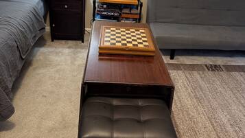 A room with a bed, a small table with a chessboard, a bench, a lamp, and a couch.
