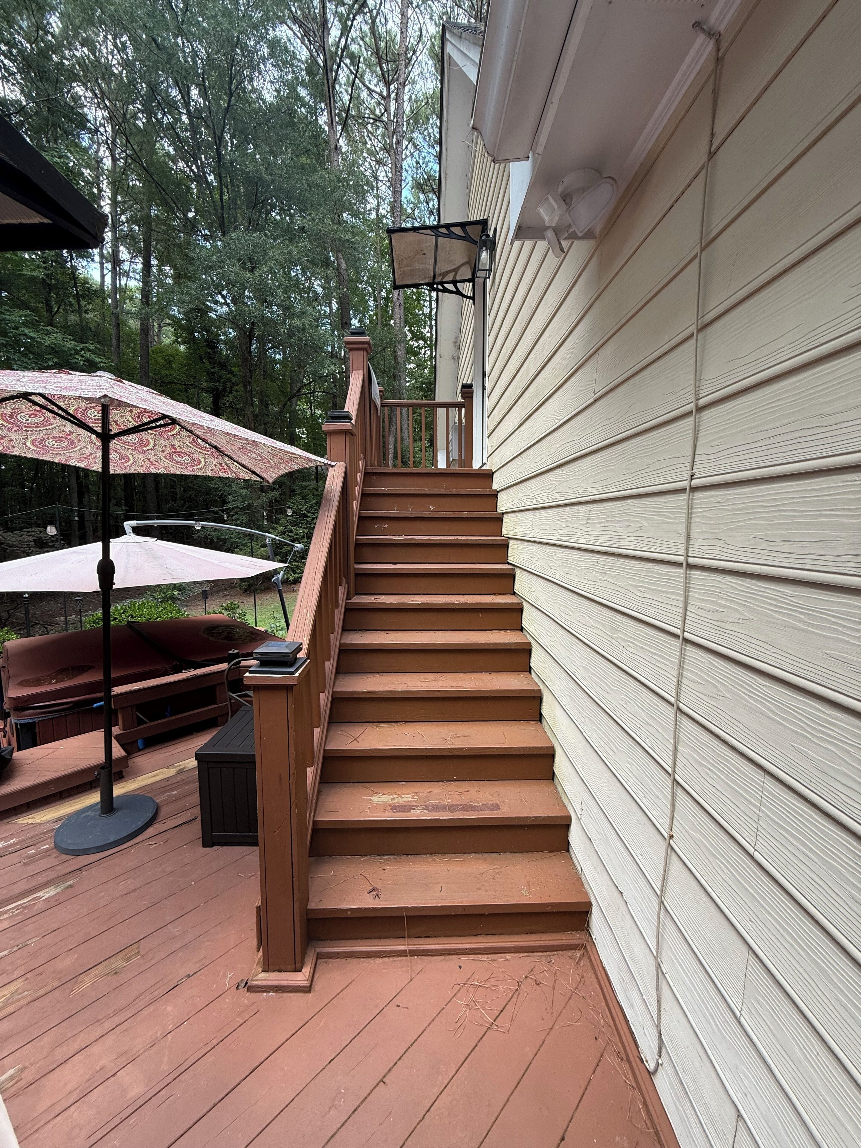 A wooden deck with a staircase leading to a covered area, surrounded by trees.