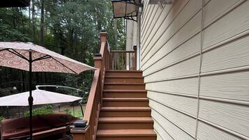 A wooden deck with a staircase leading to a covered area, surrounded by trees.