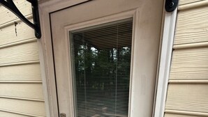 Una puerta blanca con un panel de vidrio, un pomo metálico y un pequeño dispositivo electrónico en el marco.