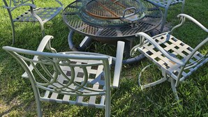 A round metal table with chairs, surrounded by a grassy yard.