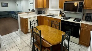 A compact kitchen with wooden cabinets, a microwave, a stove, and a dining table with chairs.