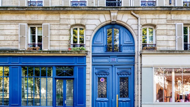 A building facade with a prominent blue door and windows, featuring a traditional architectural style with stone walls and shutters.