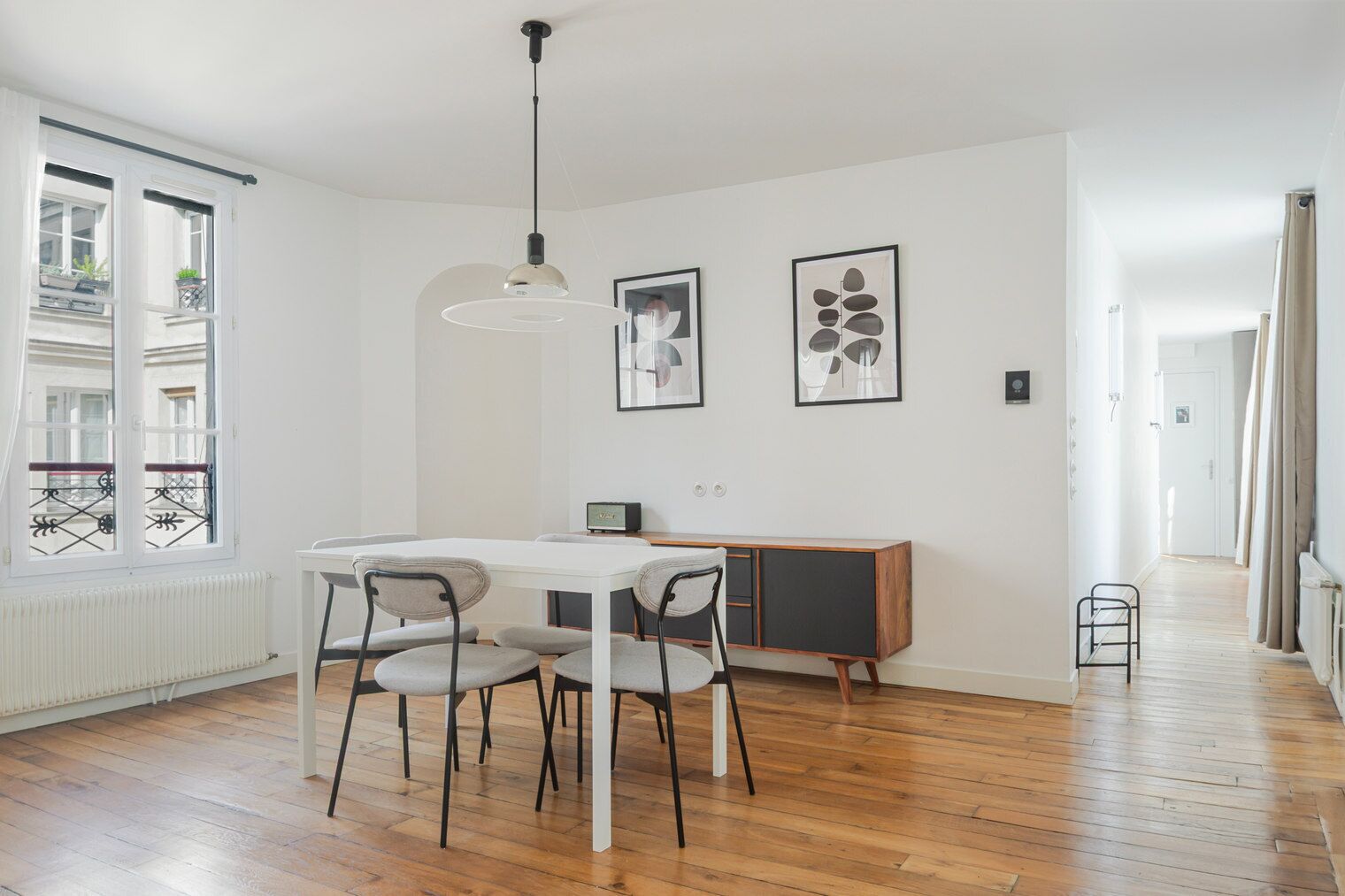 Een moderne eethoek met een witte tafel en stoelen, een hanglamp en een houten vloer.