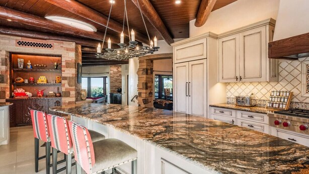Una cocina amplia con una isla grande, encimeras de granito y muebles de cocina blancos.
