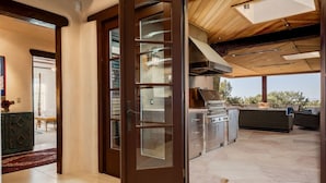 Puerta corredera de vidrio abierta que da a un patio exterior con una parrilla y asientos.