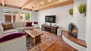 A living room with a sofa, coffee table, TV, fireplace, and a patterned rug. - Casa de Vida - Huge Yard, Hot Tub (Santa Fe)