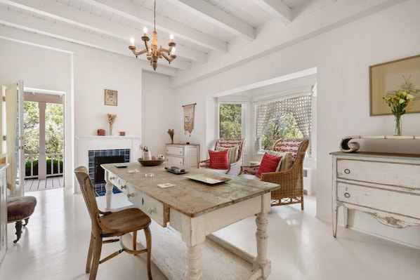Una habitación amplia con una gran mesa de madera, sillas de mimbre, una chimenea blanca y un candelabro.