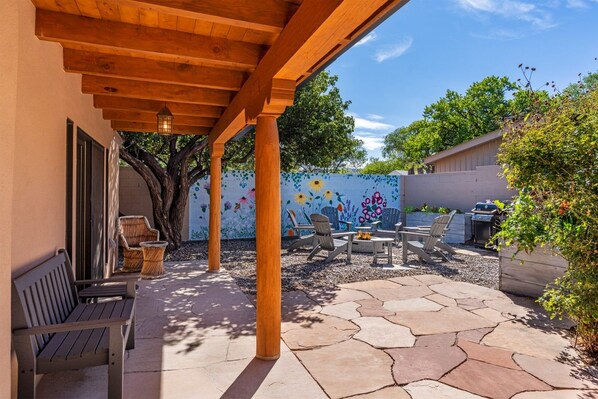Un patio al aire libre con una pérgola, zona de estar y un mural decorativo.