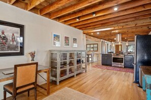A spacious kitchen with wooden beams, a dining area with a wooden table and chairs, and a kitchen island with glass doors.