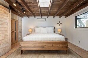 A bedroom with a wooden bed, two bedside lamps, a cross on the wall, and a window.