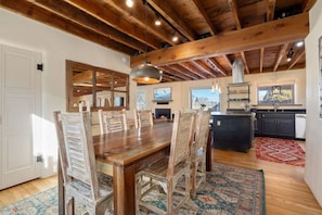A dining area with a wooden table and chairs, a kitchen with dark cabinets, and a patterned rug.