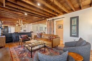 A spacious living area with a high ceiling, wooden beams, a sofa, a coffee table, and a rug.