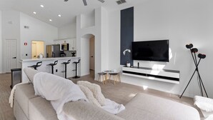 Un soggiorno moderno con un divano, televisione e una cucina sullo sfondo.