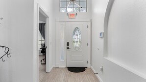 Un corridoio con una porta bianca, una finestra a vetri colorati e un lampadario al soffitto.