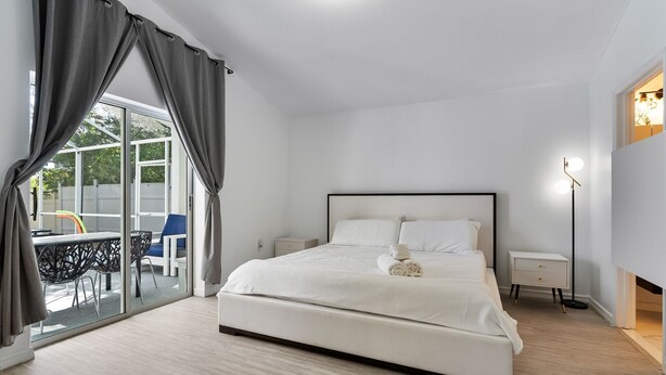 Una camera da letto con un letto grande, un comodino, una lampada e vista su uno spazio esterno con tavolo e sedie tramite una porta in vetro.
