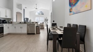 Una cucina moderna con mobili bianchi, un'area pranzo con tavolo e sedie, e un'ampia finestra con vista sul cielo.