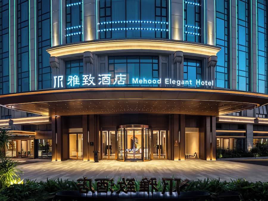 The exterior of the Mehood Elegant Hotel with a modern design, featuring a curved entrance and illuminated signage.