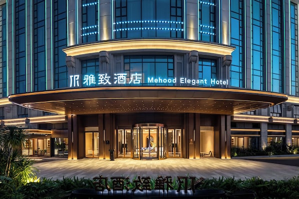 Fachada del elegante Hotel Mehood, con un diseño moderno que destaca su entrada curva y señalización iluminada.