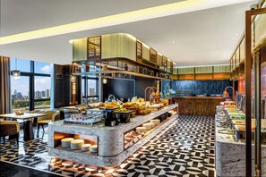 Un moderno vestíbulo de hotel con zona de buffet, asientos y vistas a la ciudad.