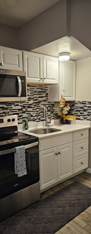 A kitchen with white cabinets, a stainless steel microwave, a black stove, a sink, and a decorative vase with flowers.