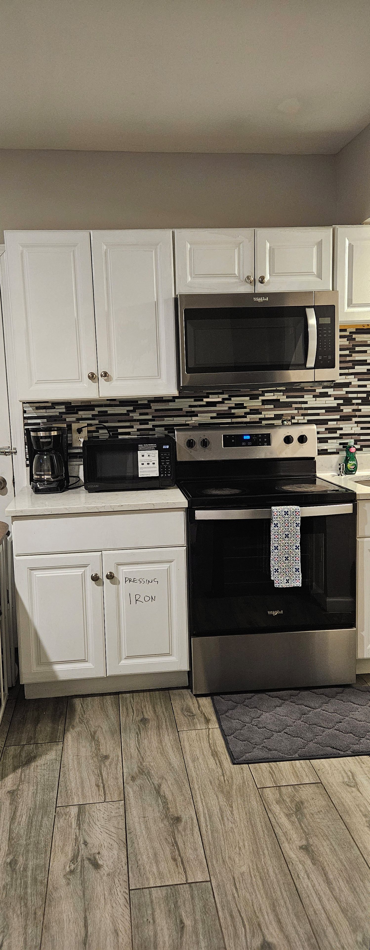 A kitchen with white cabinets, a stainless steel microwave, a stove, and a coffee maker.