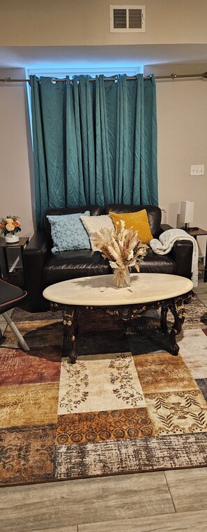 Un salon avec un canapé en cuir noir, une table basse ronde et une variété de tapis à motifs.
