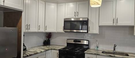 A modern kitchen with white cabinets, a stainless steel refrigerator, a microwave, and a gas stove.