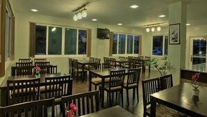A spacious dining area with multiple tables and chairs, large windows, ceiling lights, and a television. - Hanan Hotel Tagaytay (Tagaytay)