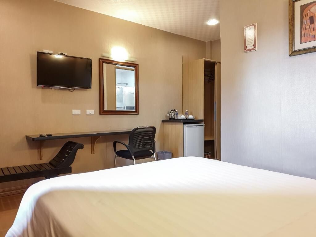 A hotel room with a bed, a desk with a chair, a television, a mirror, and a small kitchenette.