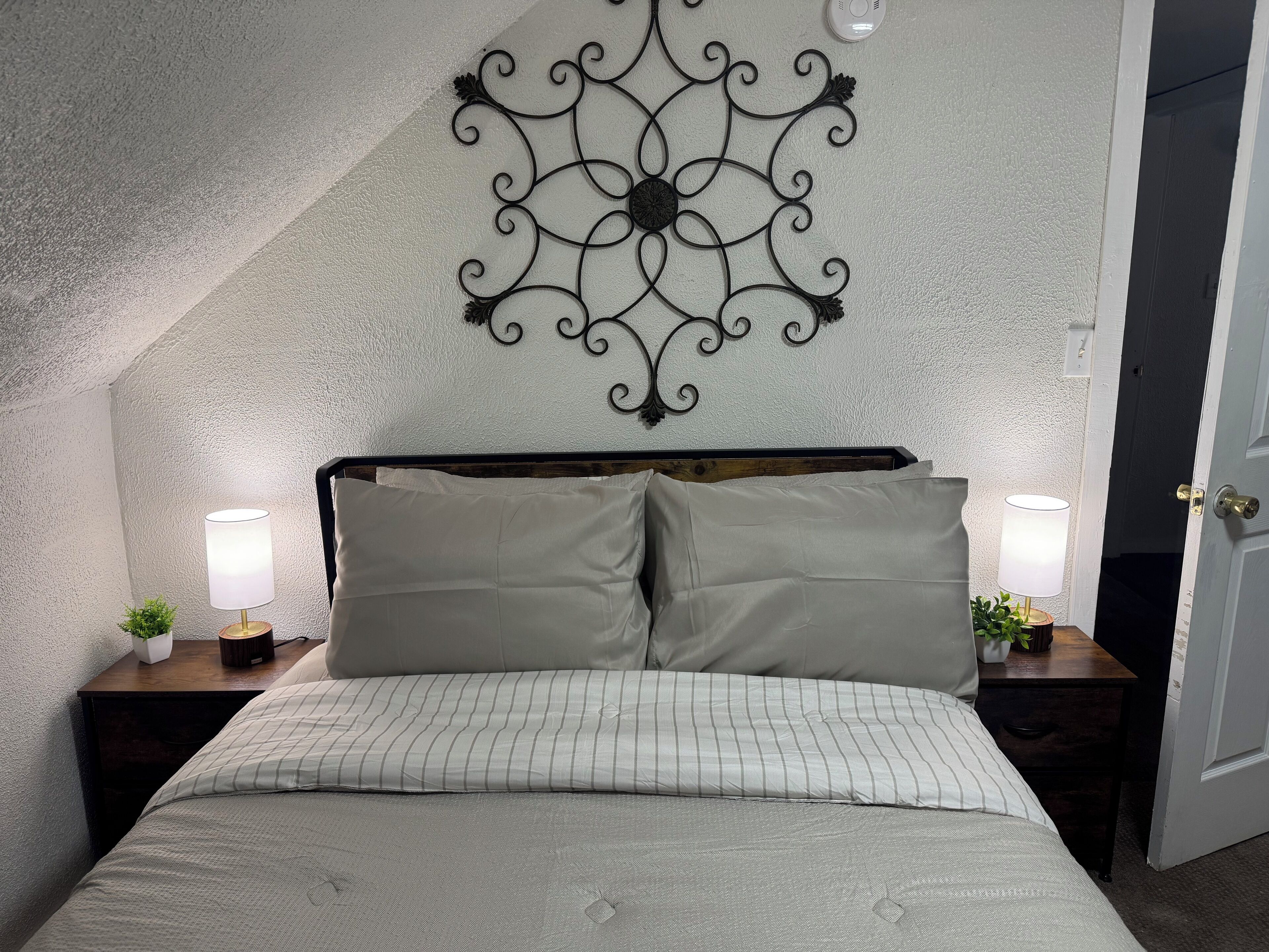 A bedroom with a sloped ceiling, a decorative wall piece, two bedside tables with lamps, and a bed with striped bedding.