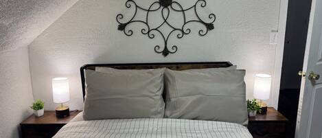 A bedroom with a sloped ceiling, a decorative wall piece, two bedside tables with lamps, and a bed with striped bedding.