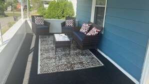 Eine überdachte Veranda mit Korbmöbeln, einem gemusterten Teppich und Blick ins Viertel.