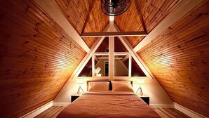 A bedroom with a sloped ceiling, wooden walls, a large bed, and two bedside lamps.