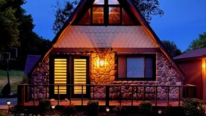 A stone cabin with a triangular roof, a stone fireplace, and a porch with a railing.