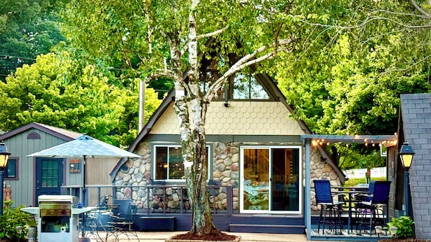 A stone house with a patio, outdoor seating, and a large tree in front.