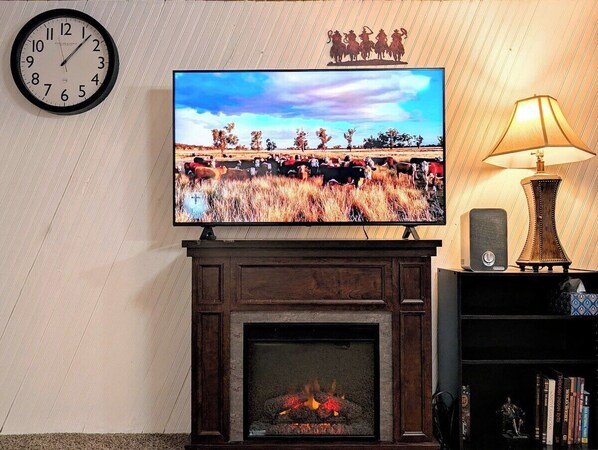 A fireplace with a TV mounted above it, a clock on the wall, and a lamp on a side table. - 5 bedrooms 2 baths walking distance to State Fair (Des Moines)