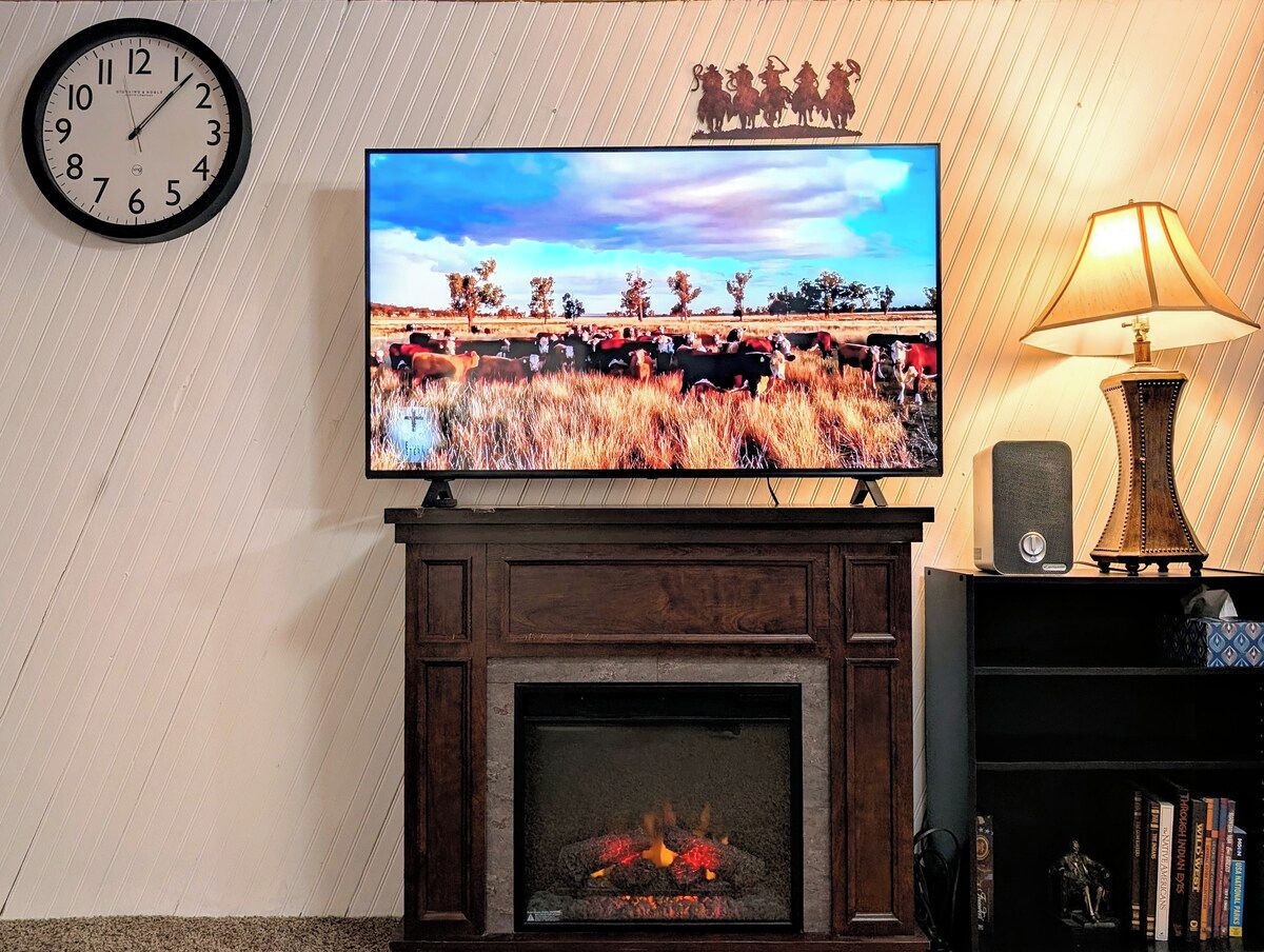 Una chimenea con un televisor montado encima, un reloj en la pared y una lámpara en una mesita.