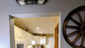 Une cuisine avec des meubles blancs, un four, un four à micro-ondes et une décoration murale en forme de roue en bois.