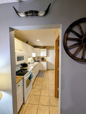 Une cuisine avec des meubles blancs, un four, un four à micro-ondes et une décoration murale en forme de roue en bois.