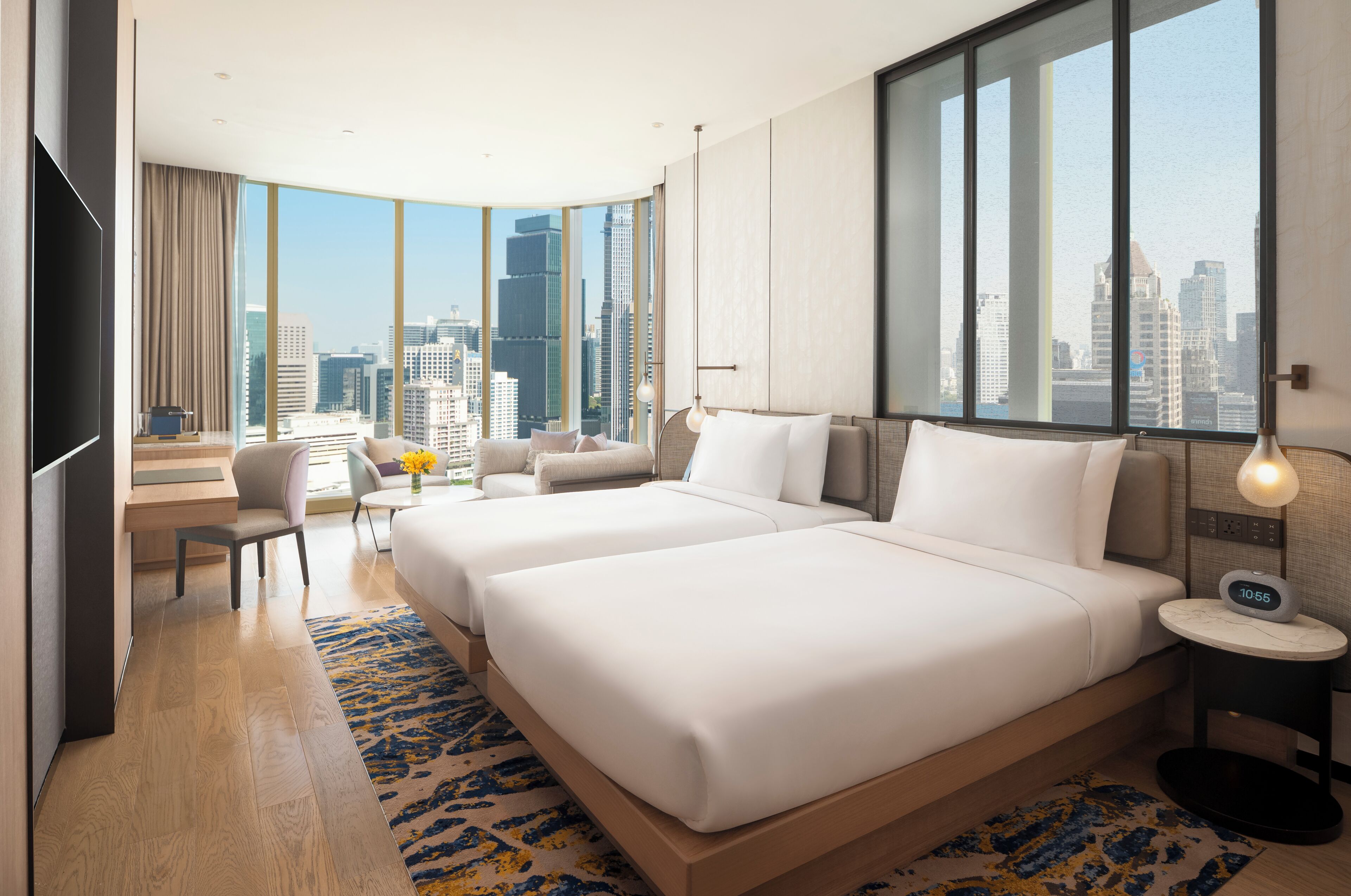 A hotel room with two beds, a desk, a chair, a TV, and a view of the city skyline.