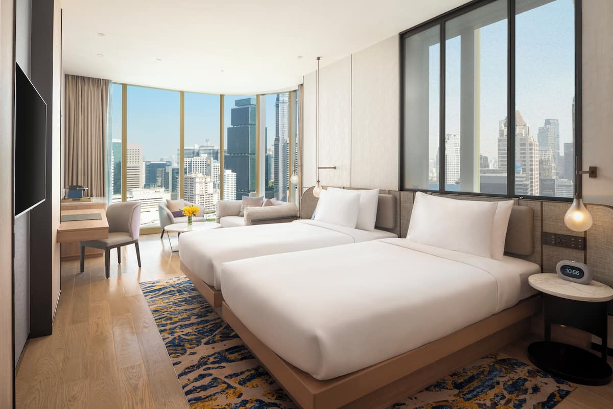 Une chambre d’hôtel avec deux lits, un bureau, une chaise, une télévision et une vue sur le panorama de la ville.