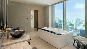 Une salle de bain moderne avec une grande baignoire, un lavabo en forme de coupe et une vue sur le paysage urbain grâce à de grandes fenêtres.