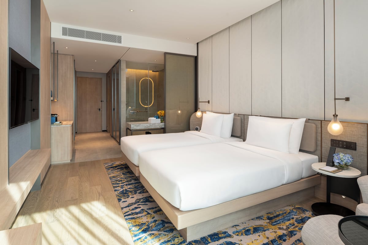 Une chambre d’hôtel moderne, dotée d’un grand lit, de tables de chevet, d’une télévision et d’une salle de bain visible à travers une porte ouverte.