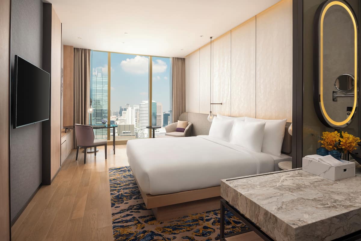 Une chambre d’hôtel moderne dotée d’un grand lit, d’une télévision à écran plat, d’une vue sur la ville, d’un bureau et d’un miroir dans la salle de bain.