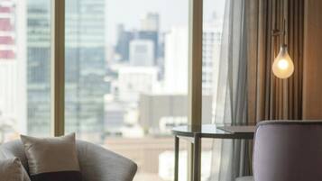 A modern room with a sofa, a round table, and a chair, with a city view through large windows and a hanging light fixture.