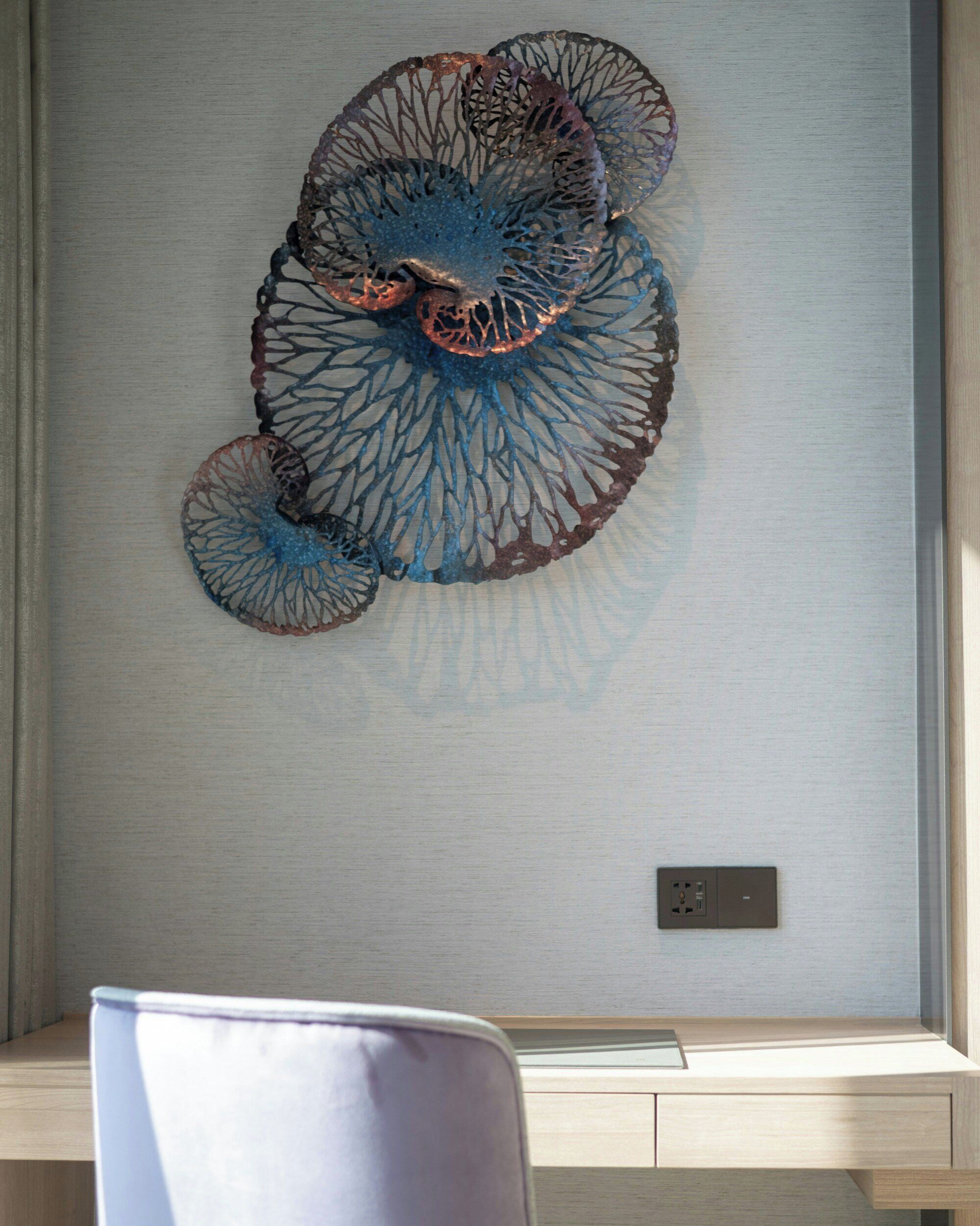 Un élément décoratif mural de forme circulaire, un bureau en bois avec une chaise et une prise de courant.