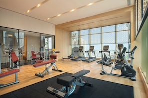 Een ruime fitnessruimte met diverse trainingsapparaten, grote ramen en een houten vloer.