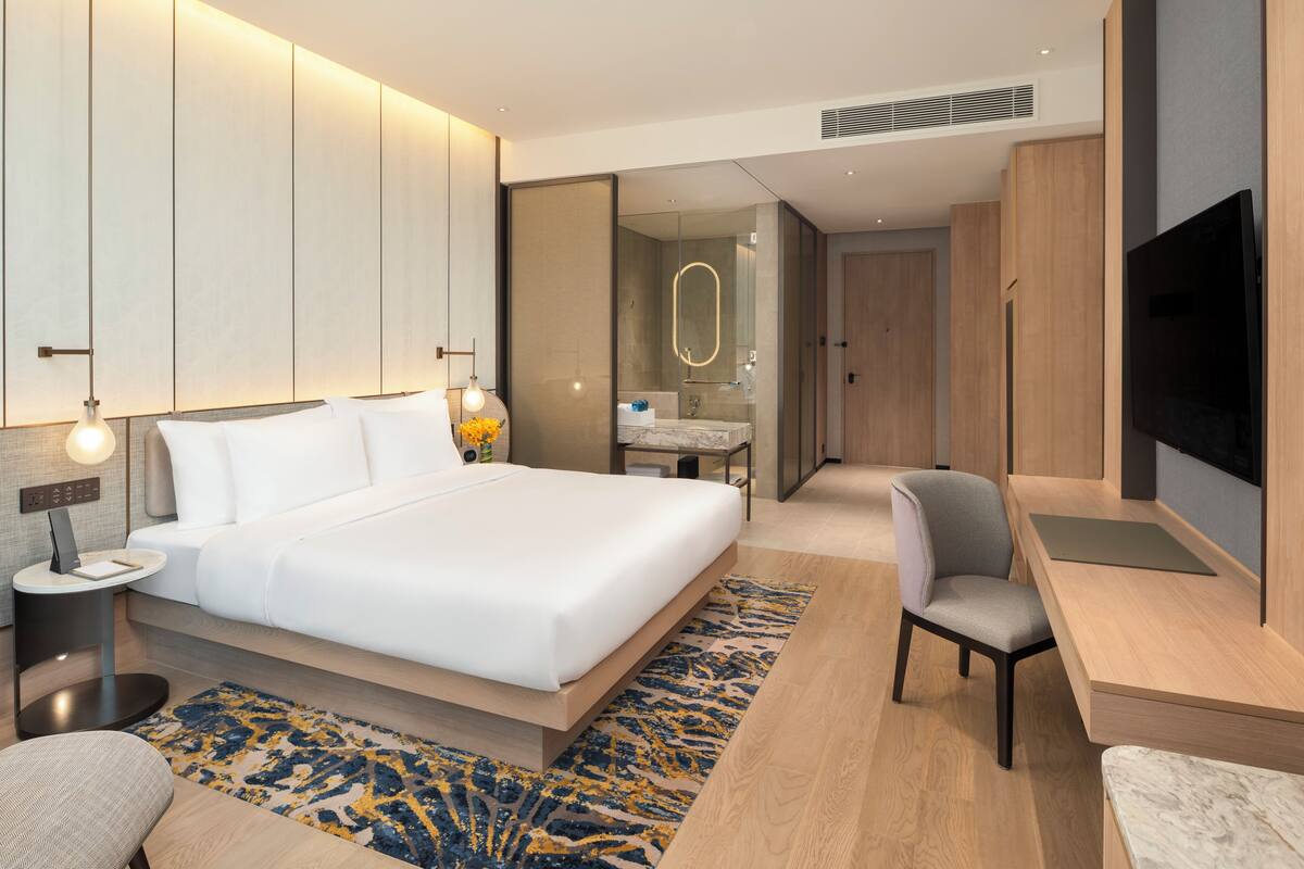 Une chambre d’hôtel moderne dotée d’un grand lit, d’un bureau, d’une chaise, d’une télévision, d’une salle de bain et d’un dressing.