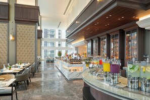Un hall d’hôtel doté d’un comptoir d’accueil en marbre, d’un espace buffet et de différents coins salon.